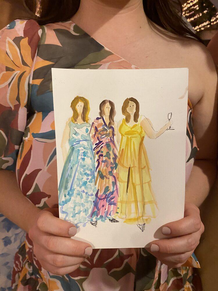 Gościni wesela trzyma swoją akwarelową ilustrację z trzema postaciami