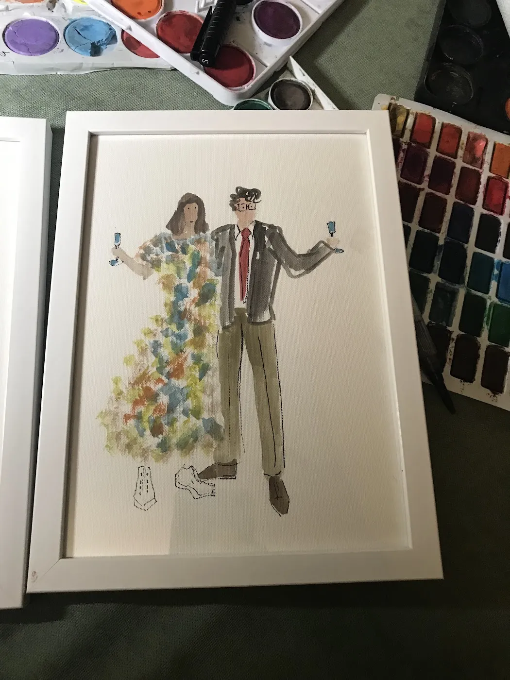 Oprawiona akwarelowa ilustracja pary obok palety farb na weselu w Sulęczynie