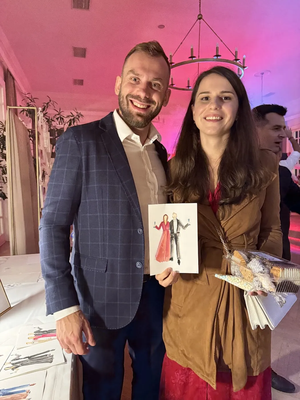 Uśmiechnięta para gości trzyma akwarelowy portret na weselu