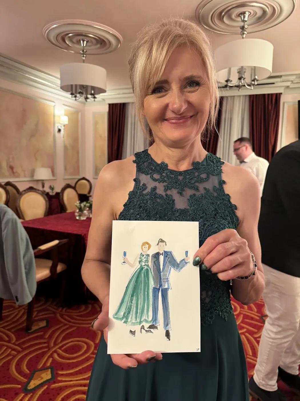 Uśmiechnięta kobieta w zielonej sukience prezentuje swój akwarelowy portret