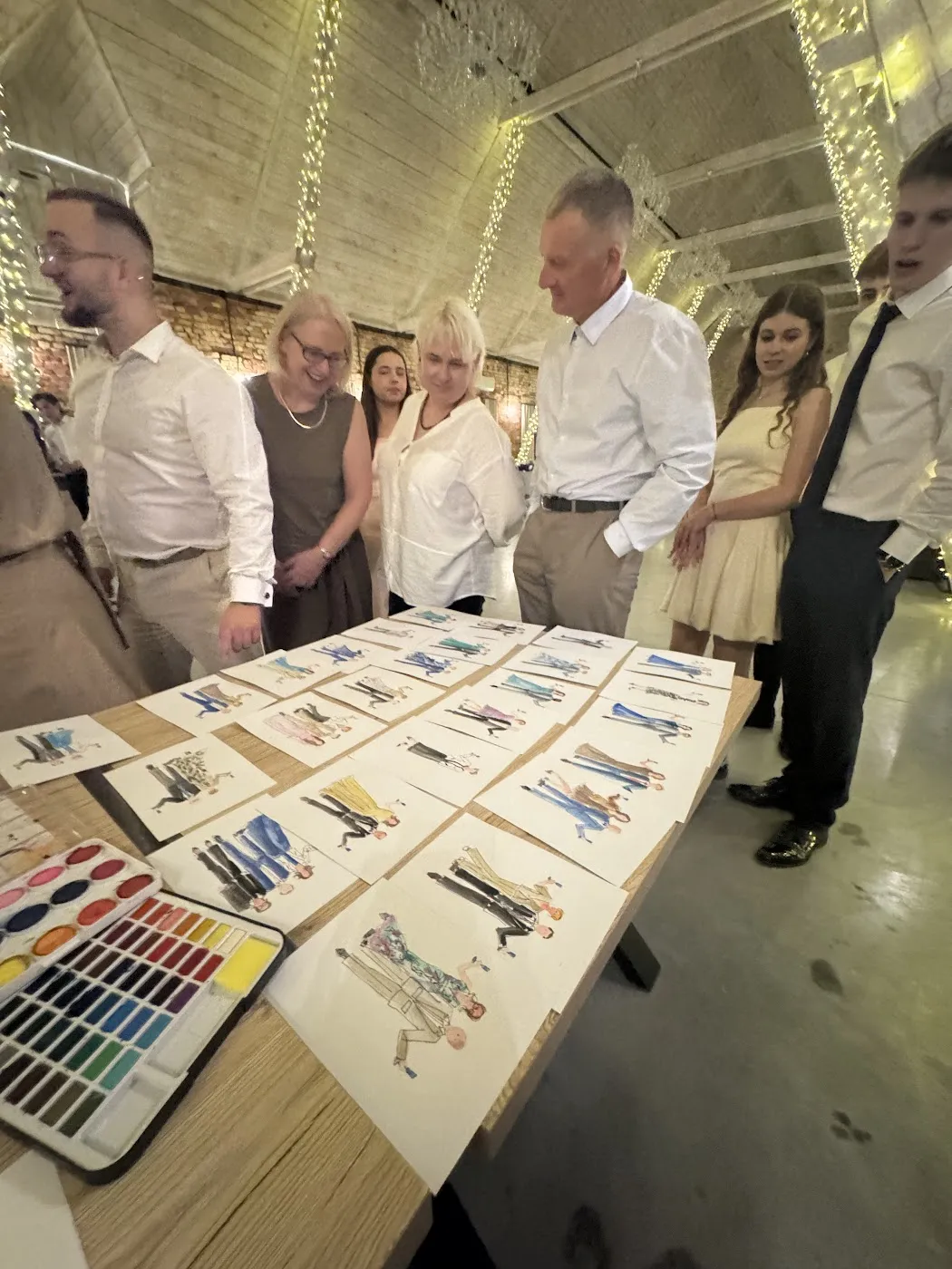 Goście przy stole z rozłożonymi ilustracjami i paletą akwareli