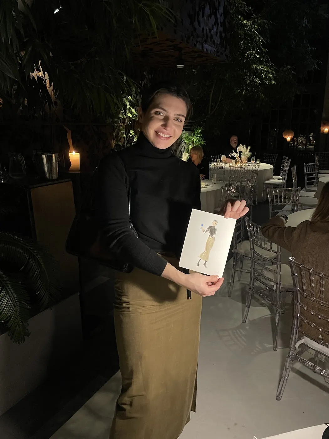 Kobieta w czarnym stroju pokazuje akwarelowy portret w Restauracji Belvedere