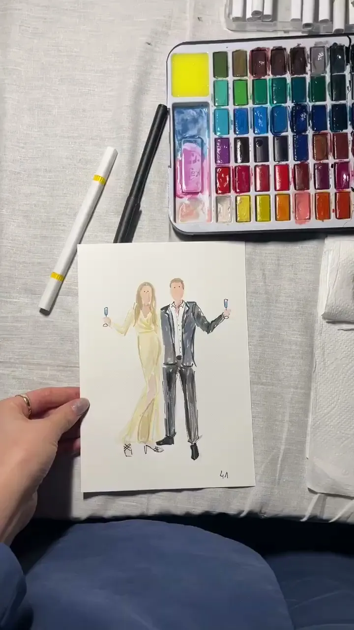 Gotowy akwarelowy portret pary gości trzymany nad stołem z farbami